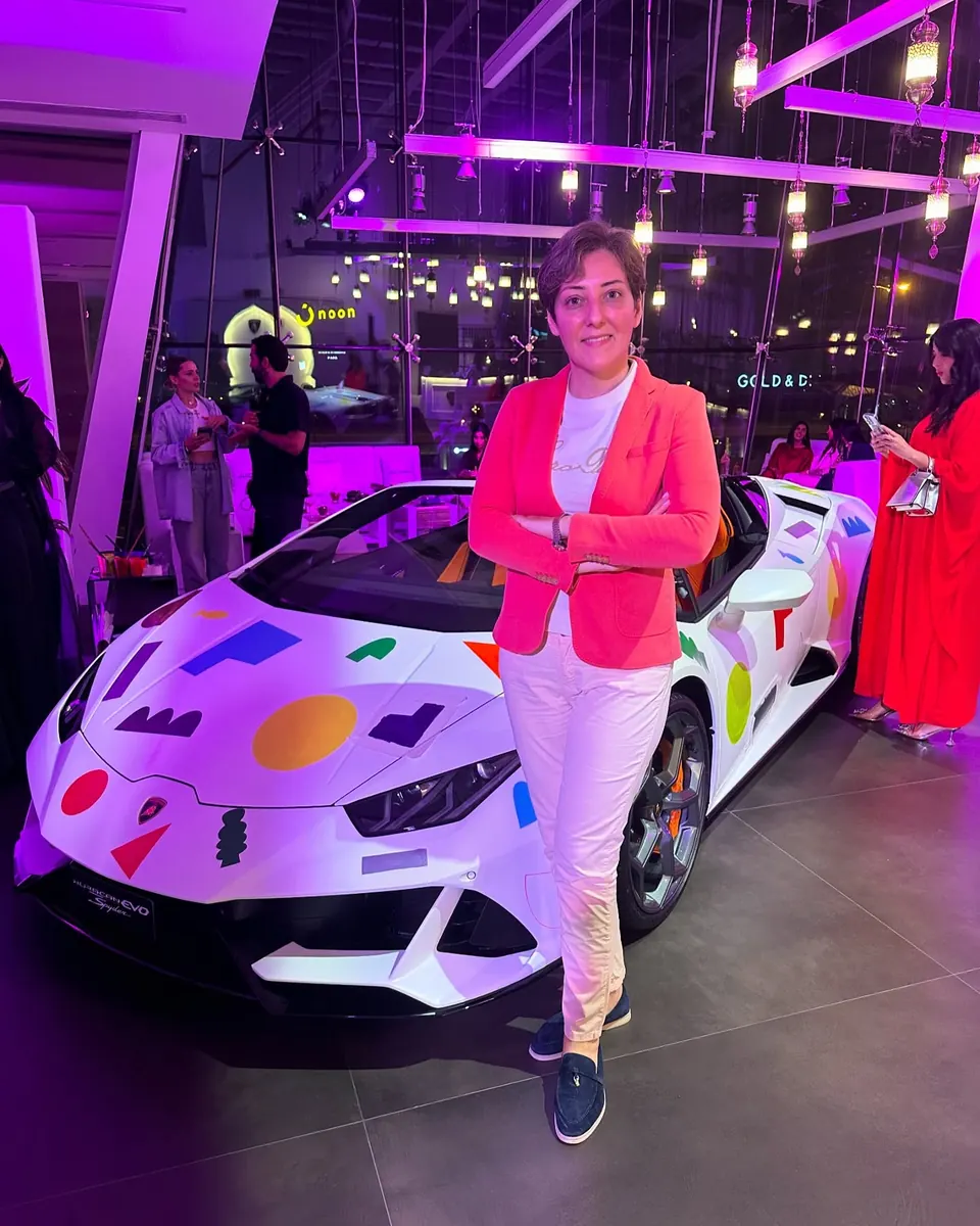 Mehrnoosh in a coral blazer beside a white Lamborghini Huracán EVO Spyder painted with colourful shapes
