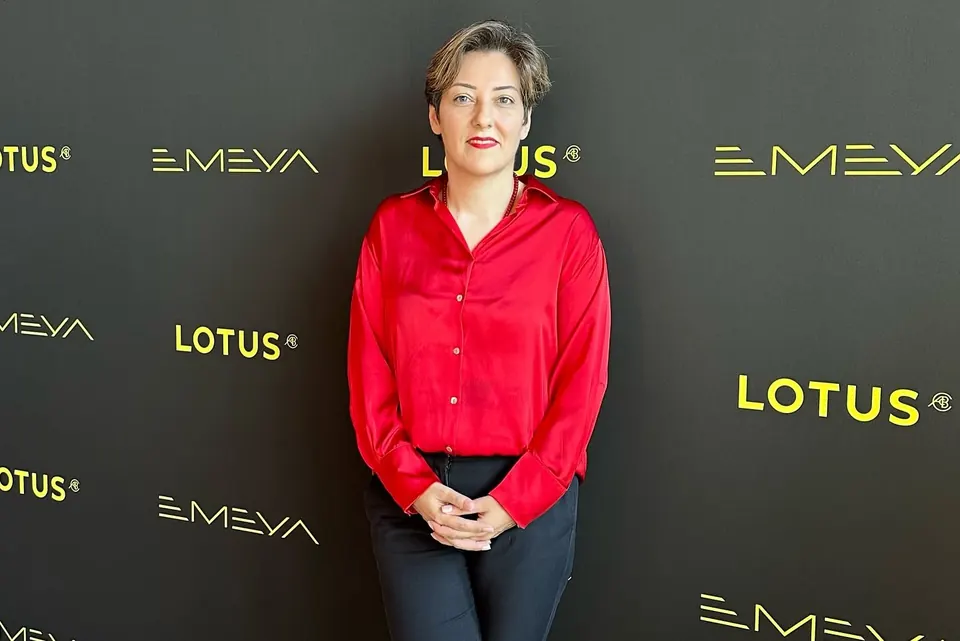 Mehrnoosh in a red satin shirt in front of a Lotus Emeya backdrop