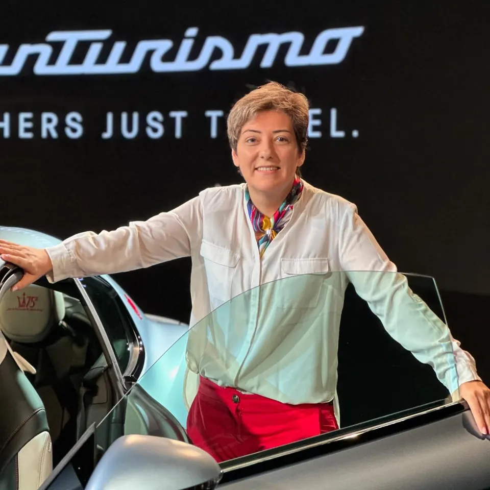Mehrnoosh smiling with her arms on the open door of a Maserati GranTurismo in front of its illuminated name