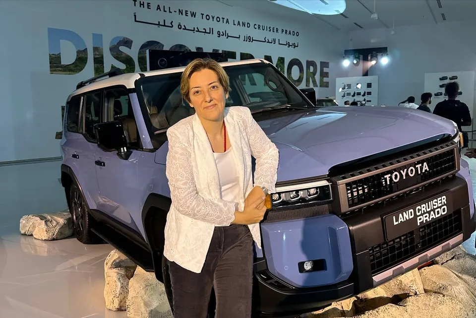 Mehrnoosh leaning on the front of a lavender Toyota Land Cruiser Prado at its launch display