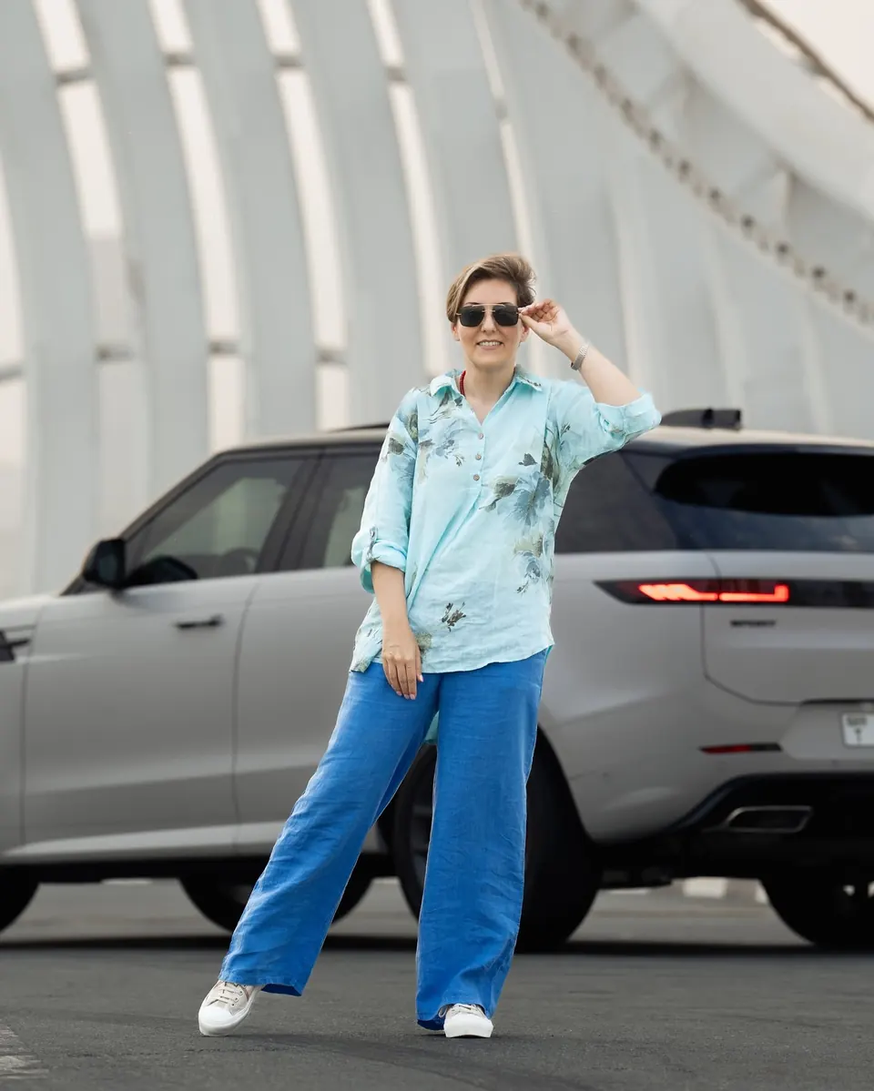 Mehrnoosh in sunglasses and a floral shirt posing beside a satin grey Range Rover Sport on a bridge