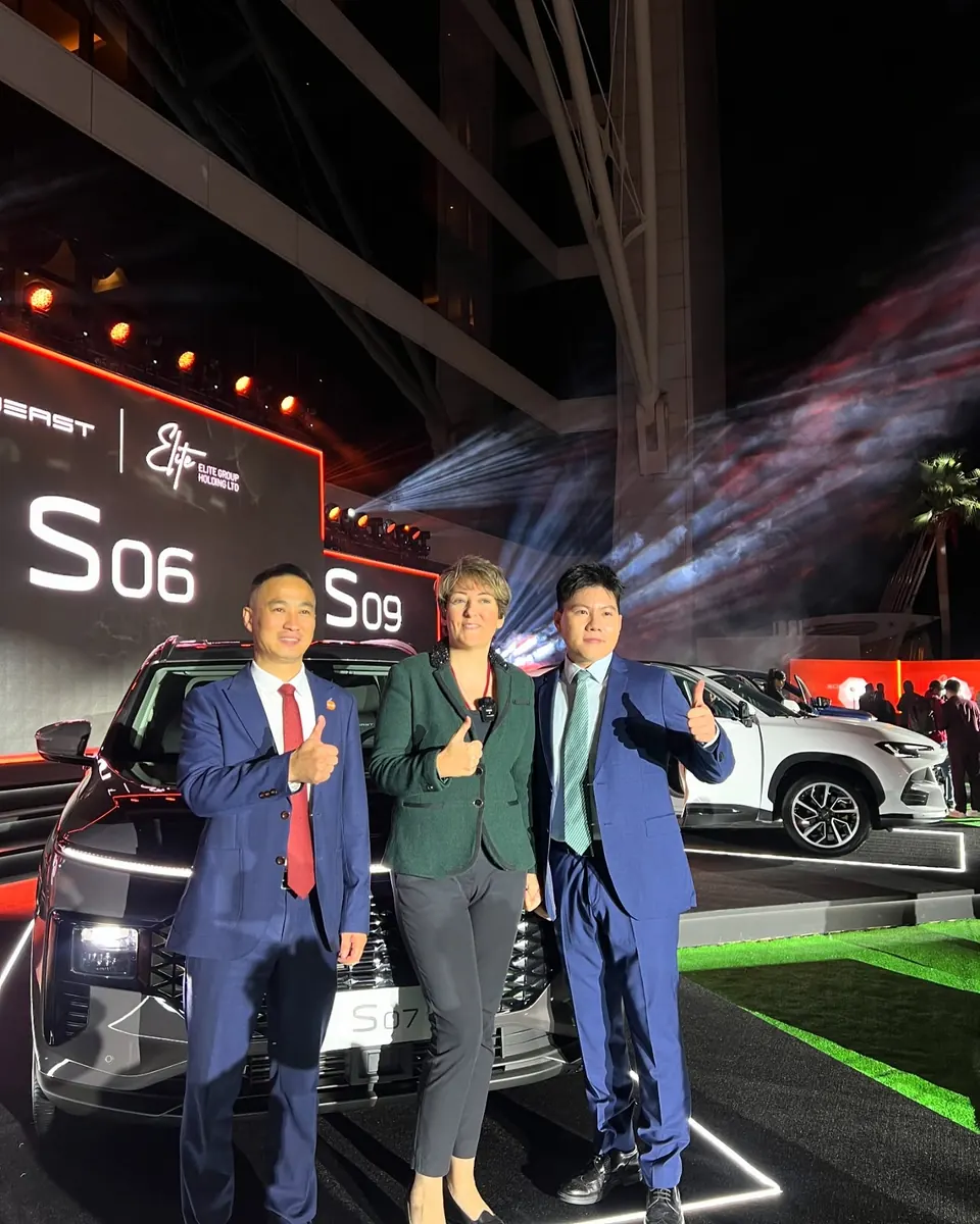 Mehrnoosh wearing a microphone, giving a thumbs up with two guests in front of a Soueast S07 at a night launch
